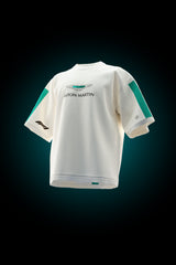 A white short-sleeve t-shirt with teal and black accents, featuring the Aston Martin wing logo and 'ASTON MARTIN' text on the chest, displayed against a dark background with a blue glow.