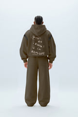 Person wearing a brown hoodie and pants with text on the back, standing against a white background