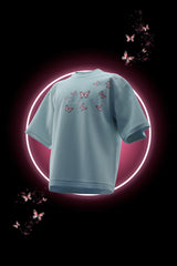 Light blue t-shirt with butterfly patterns on a black background with butterfly graphics.